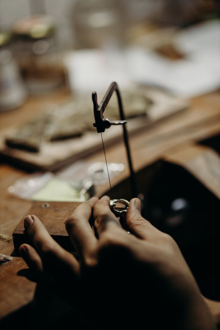 services-02 Skilled artisan working with jeweler's saw to craft intricate designs on a wooden workbench.