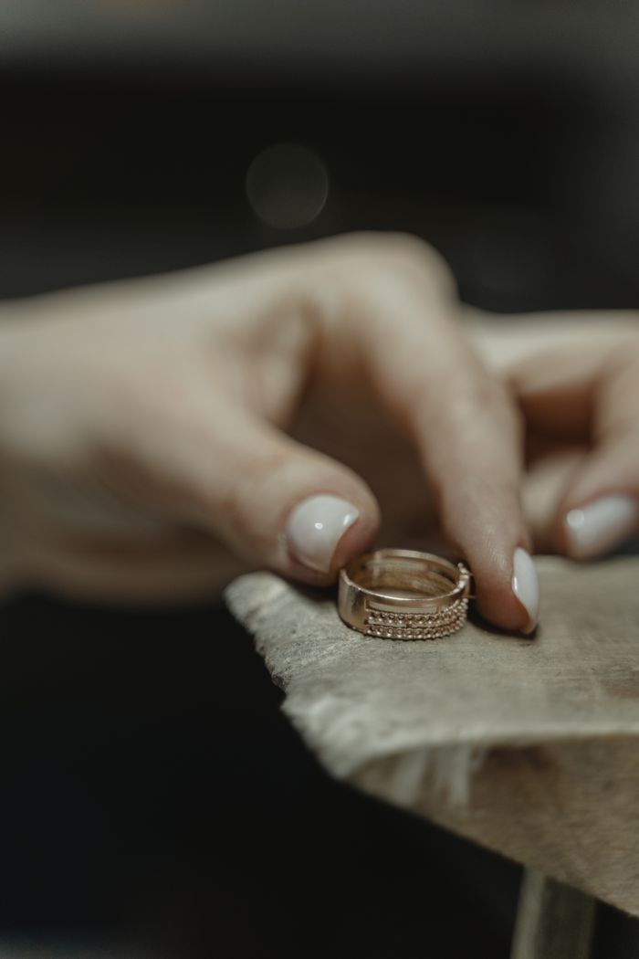 Close-up of a gold diamond ring being held by a hand with polished nails, showcasing luxury and elegance.