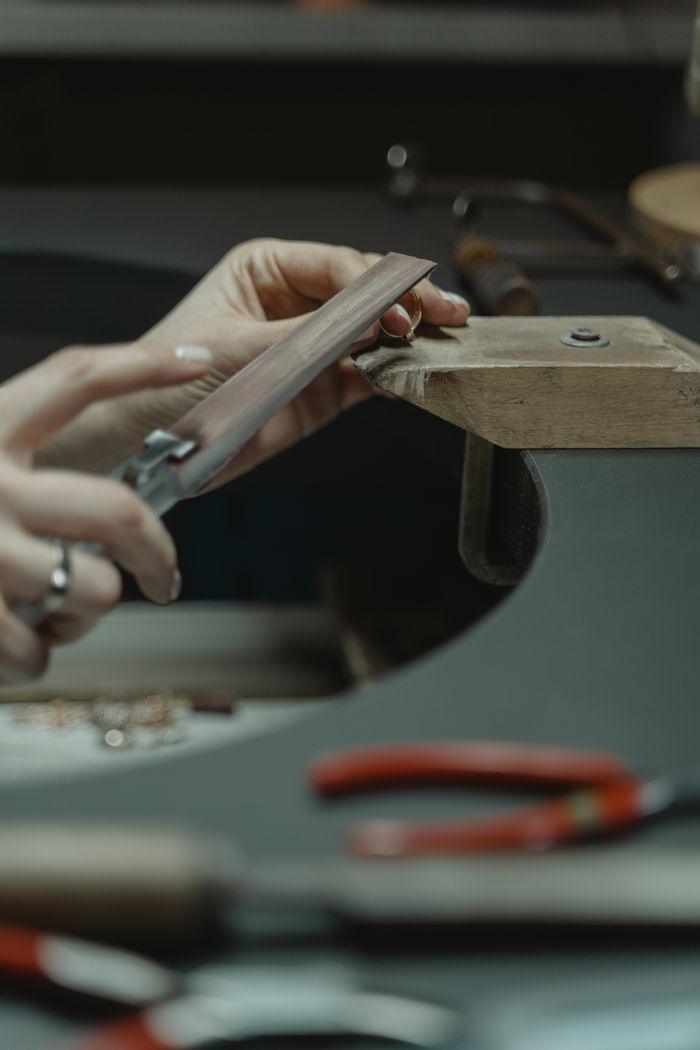 services-01 Close-up of a jeweler using a file on metal, crafting delicate jewelry pieces in an artisan workshop.